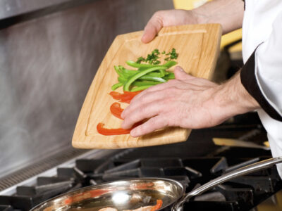 A professional Chef's hands adding fresh vegetables to a saute pan with seafood.